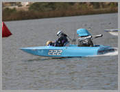 Blue speedboat numbered 222 racing on choppy water near shore